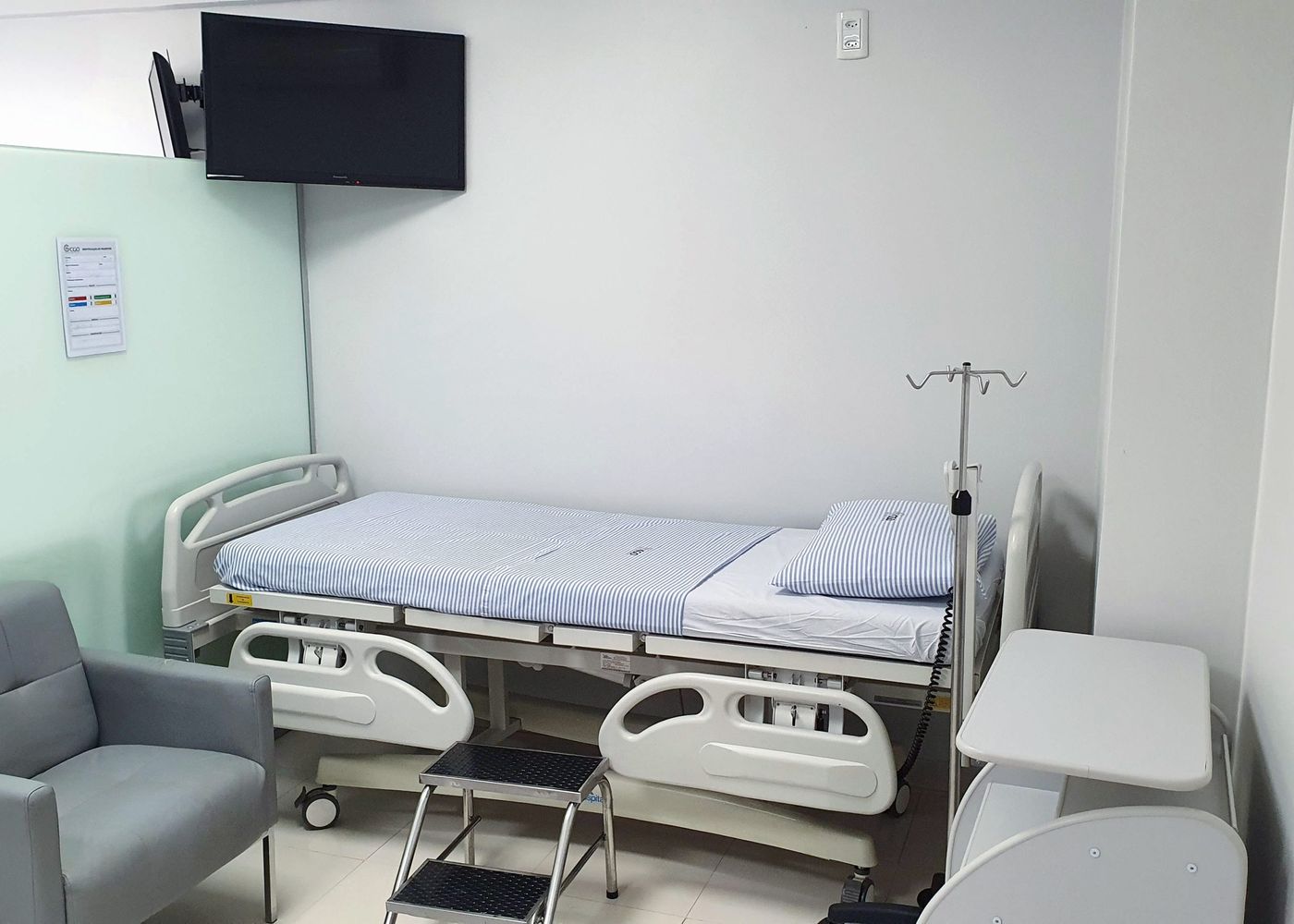 Leito do ambulatório do CEO, com poltrona de acompanhante, suporte de soro e televisor
